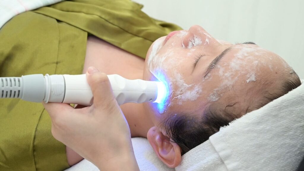 Đầu máy phát ánh sáng xanh được đưa lên khuôn mặt khách đang phủ lớp gel trong — Phòng khám Chuyên khoa Da liễu Lona Skin Lab, Cần Thơ